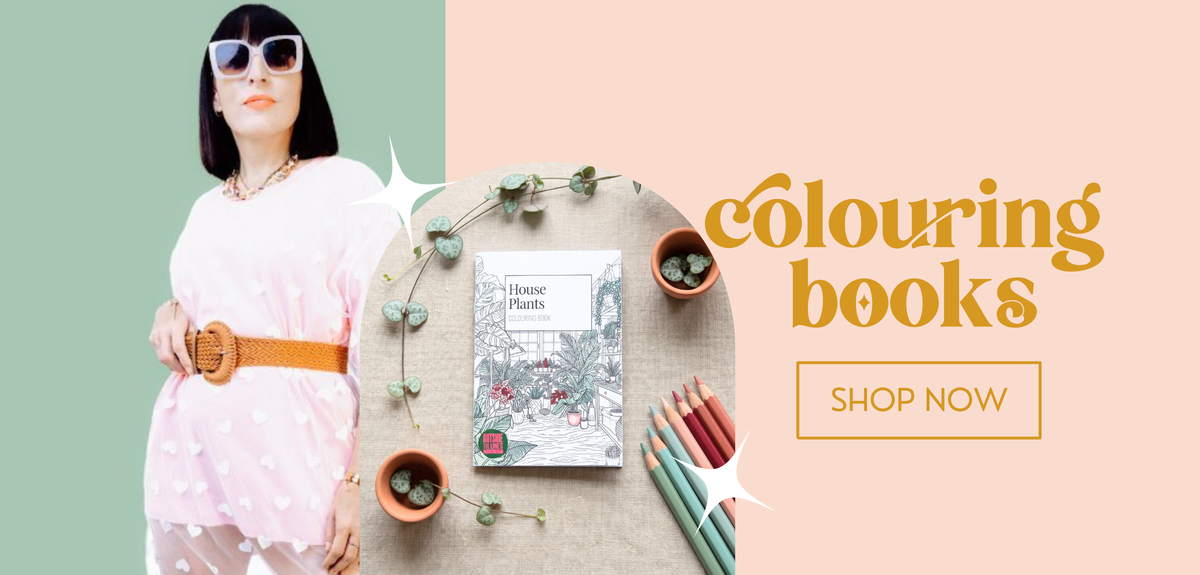 Promotional banner for a colouring book, featuring a woman in a pink dress and sunglasses on the left, and a styled flat-lay of a 'House Plants' colouring book with colored pencils and small pots on a beige surface on the right. The background is split diagonally between sage green and peach, with the text 'colouring books' and 'SHOP NOW'.