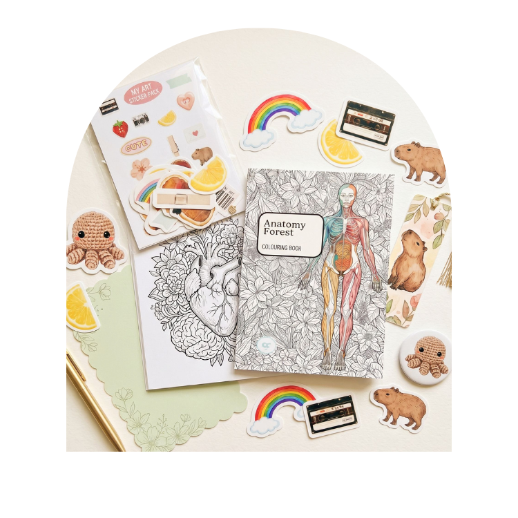 A styled flat-lay of stationery and coloring-book items arranged on a cream surface. The main product appears to be the Anatomy Forest coloring book, with additional stickers, a black-and-white line art sheet, small cards, and illustrated pieces around it.