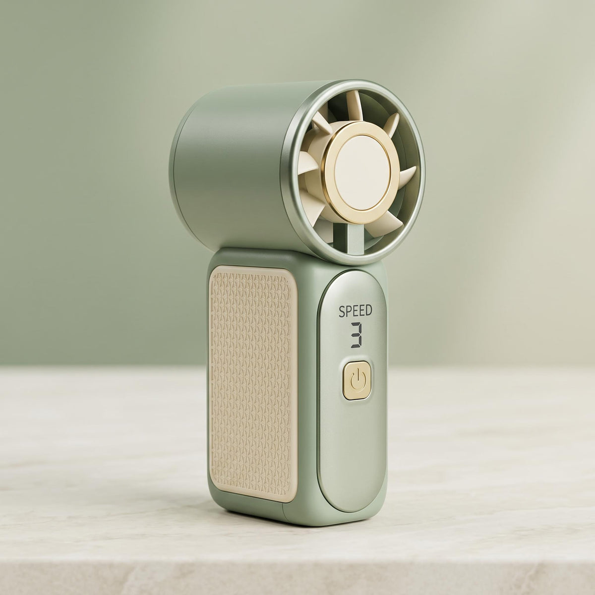 A compact handheld fan in sage green and beige, standing upright on a light marble surface against a soft sage green background.