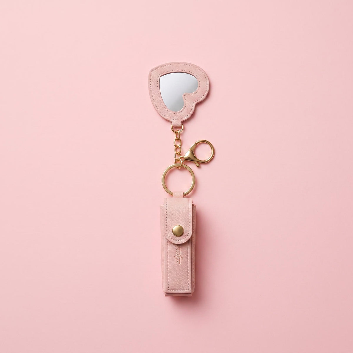 A pink faux-leather keychain organizer with an attached heart-shaped mirror and gold-tone hardware, displayed on a solid pink background.