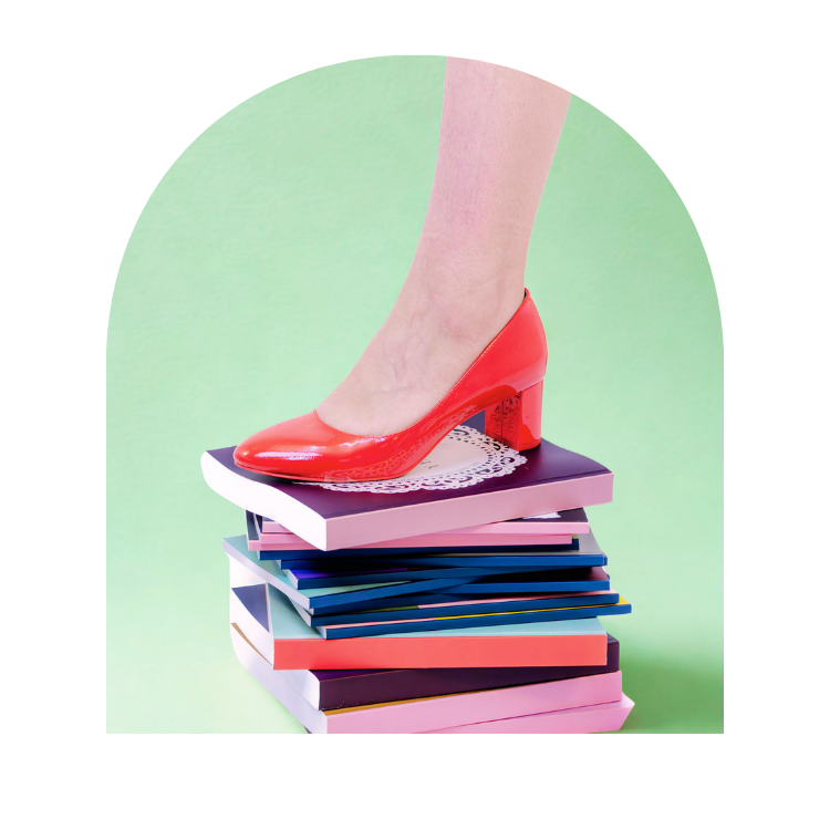 A glossy red patent leather high-heeled pump with a block heel, shown with a person's foot stepping onto a stack of colorful books against a mint green arched background.