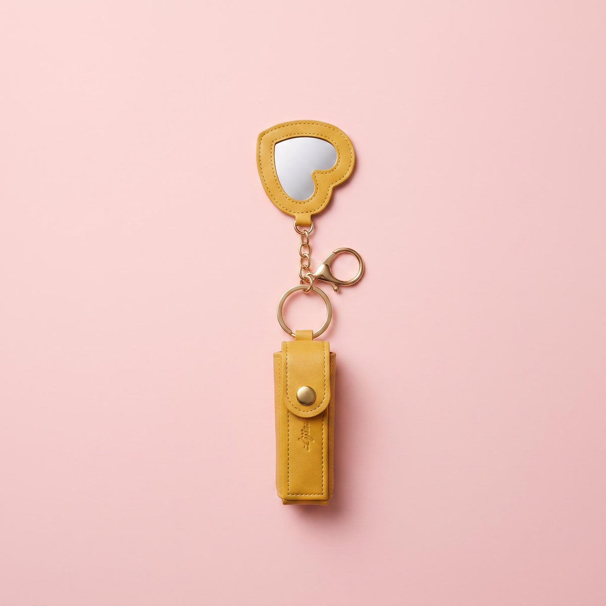A yellow leather keychain organizer with a small heart-shaped mirror and gold-tone hardware, displayed on a solid pink background.